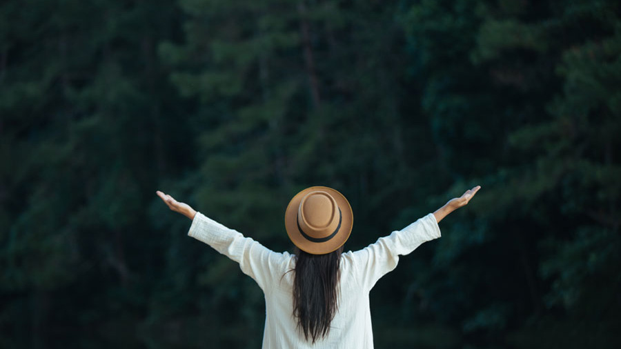 Femme de dos levant les bras face à la beauté de la forêt